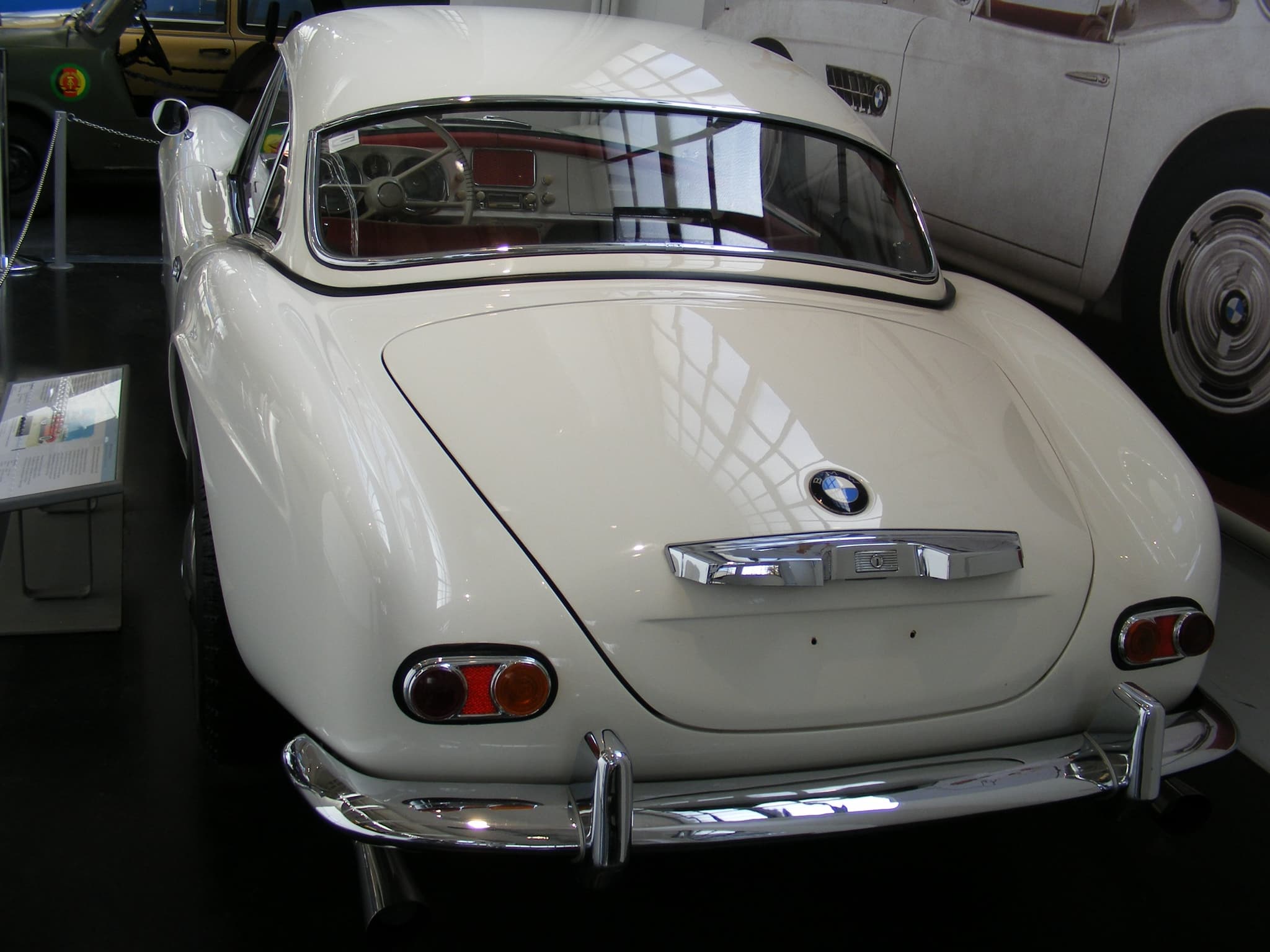The rear of a white BMW 507 with its white hardtop, showing the rear window, boot handle and twin tail lamps. Opens a larger view