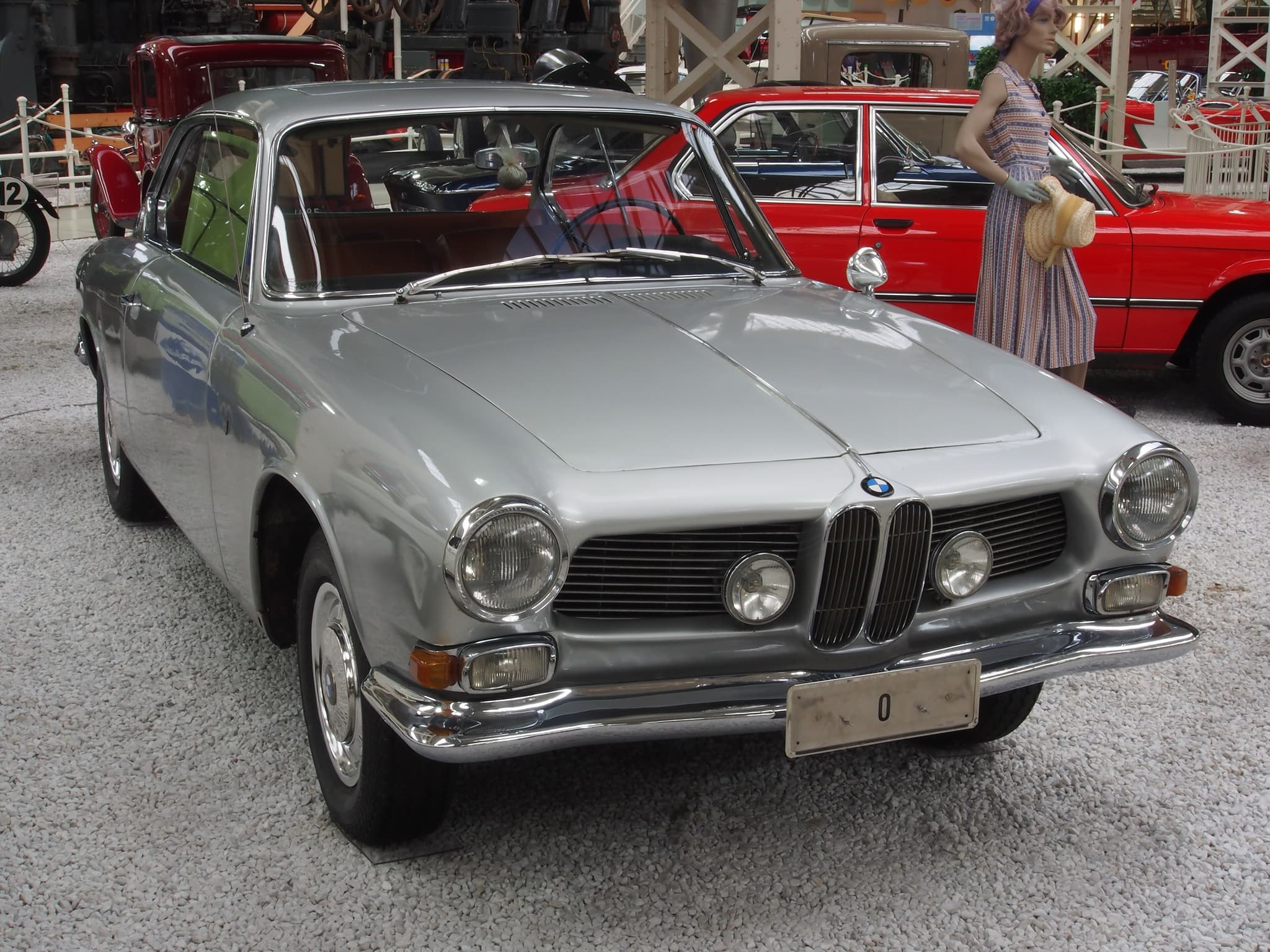 A silver BMW 3200 CS coupé with twin kidney grilles and round headlamps on a gravel museum floor.