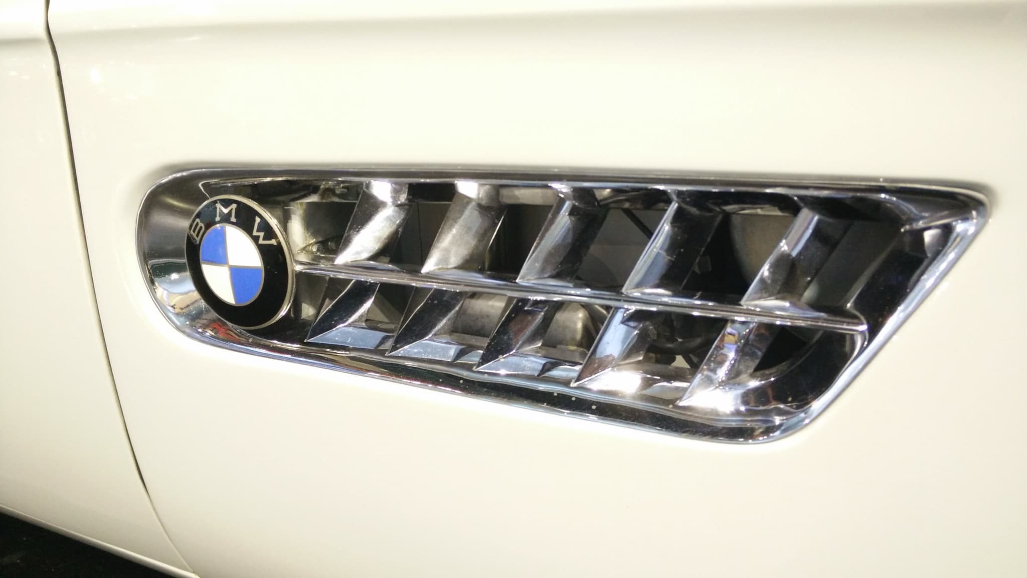 The chrome side vent with a blue-and-white BMW roundel on the white wing of a BMW 507. Opens a larger view