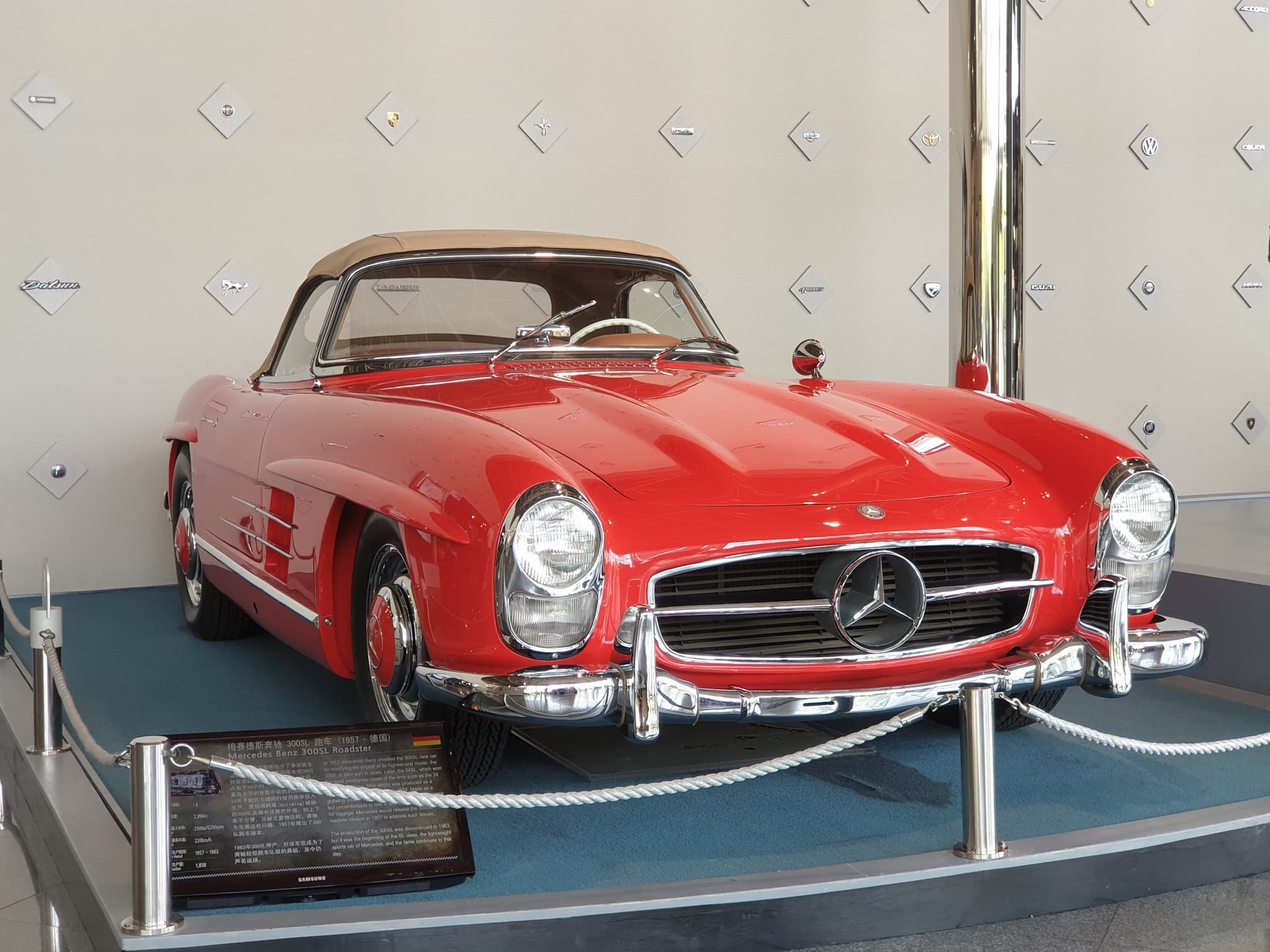 A red Mercedes-Benz 300 SL roadster with a beige hood on a roped museum plinth.