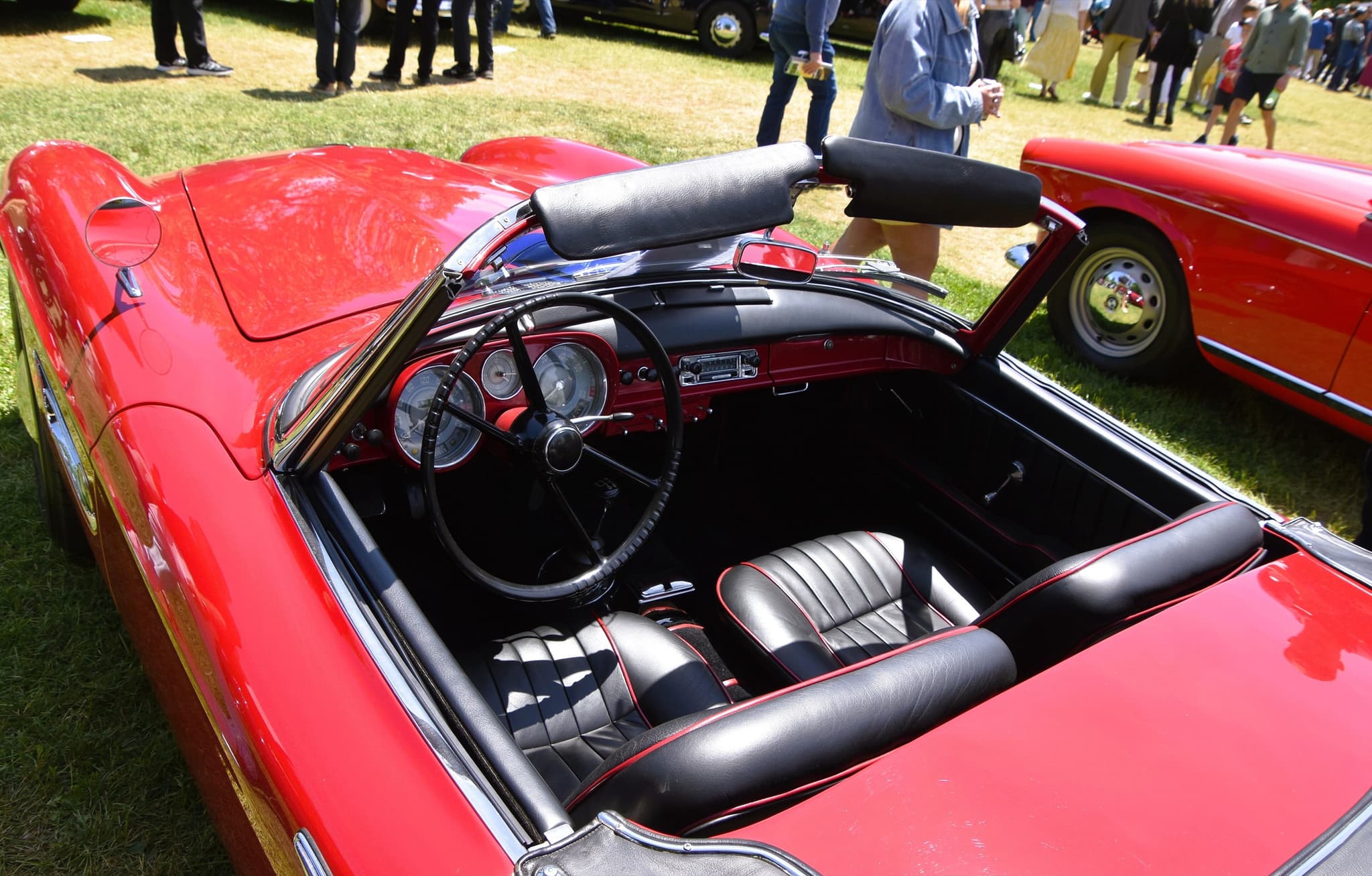 The cockpit of a red BMW 507 with black leather seats, a black steering wheel and three dials in a red dashboard. Opens a larger view