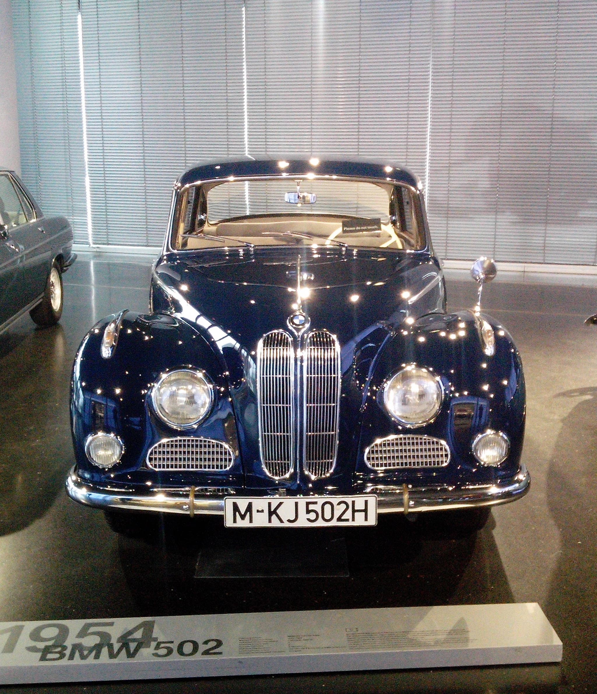 A dark blue BMW 502 saloon head-on in a museum, with a tall kidney grille between round headlamps.