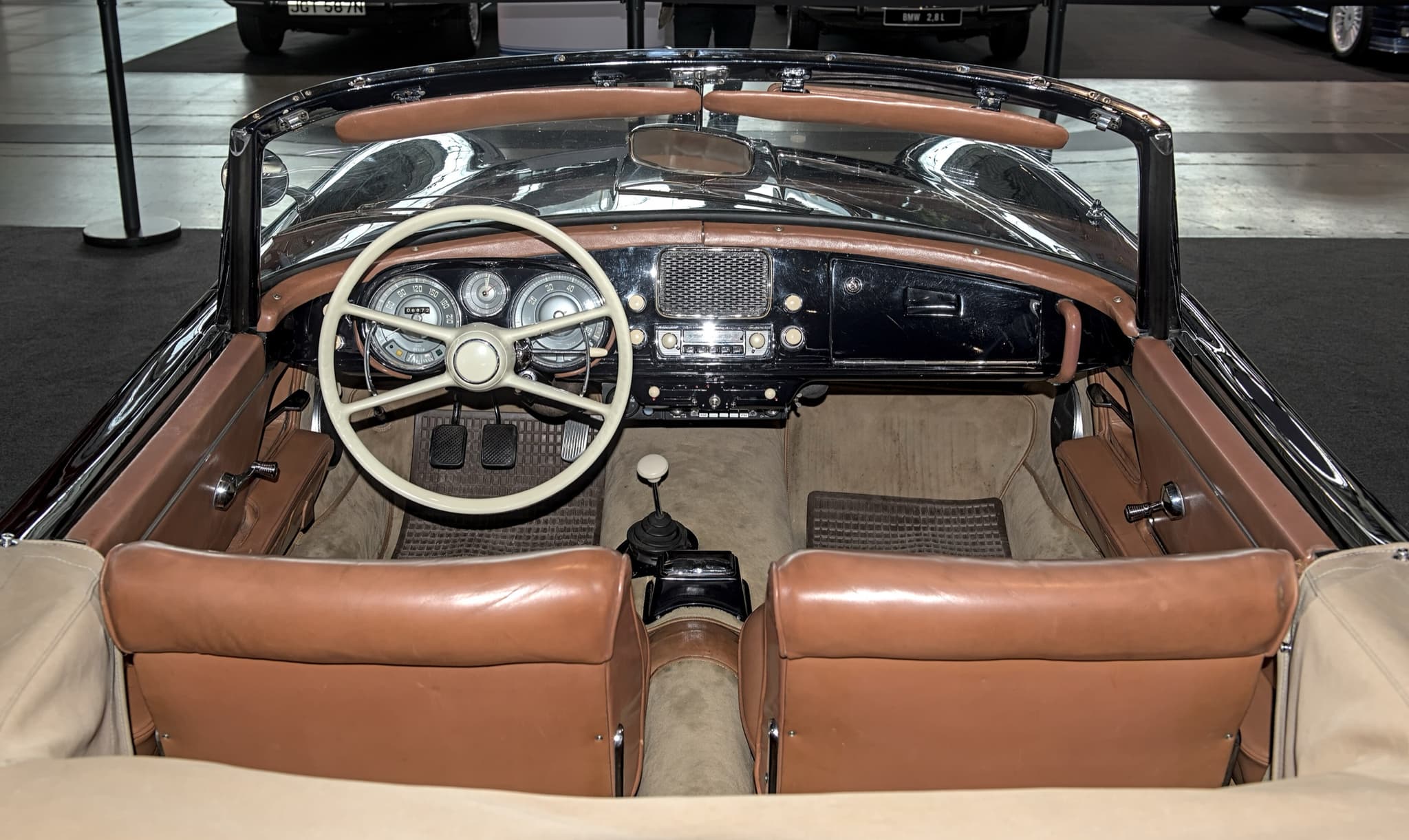 The cockpit of a black BMW 507 with brown leather seats, an ivory steering wheel and three round dials in a black dashboard. Opens a larger view